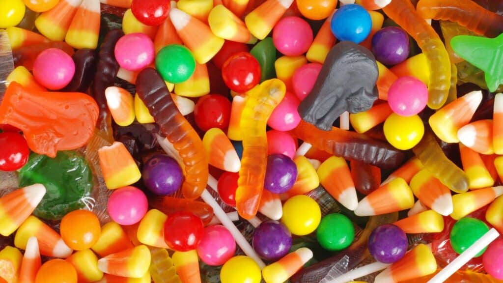 A variety of assorted Halloween candies, including candy corn, gummy worms, gumballs, and a black skull-shaped gummy.