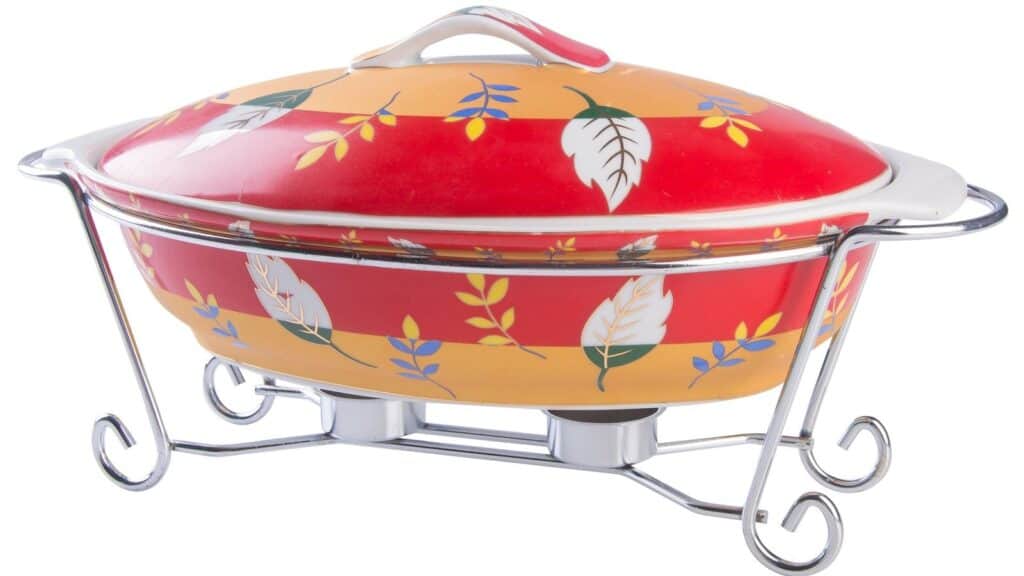Oval ceramic casserole dish with a red and yellow leaf pattern, resting in a chrome wire warming stand, reminiscent of QVC and HSN impulse buys.