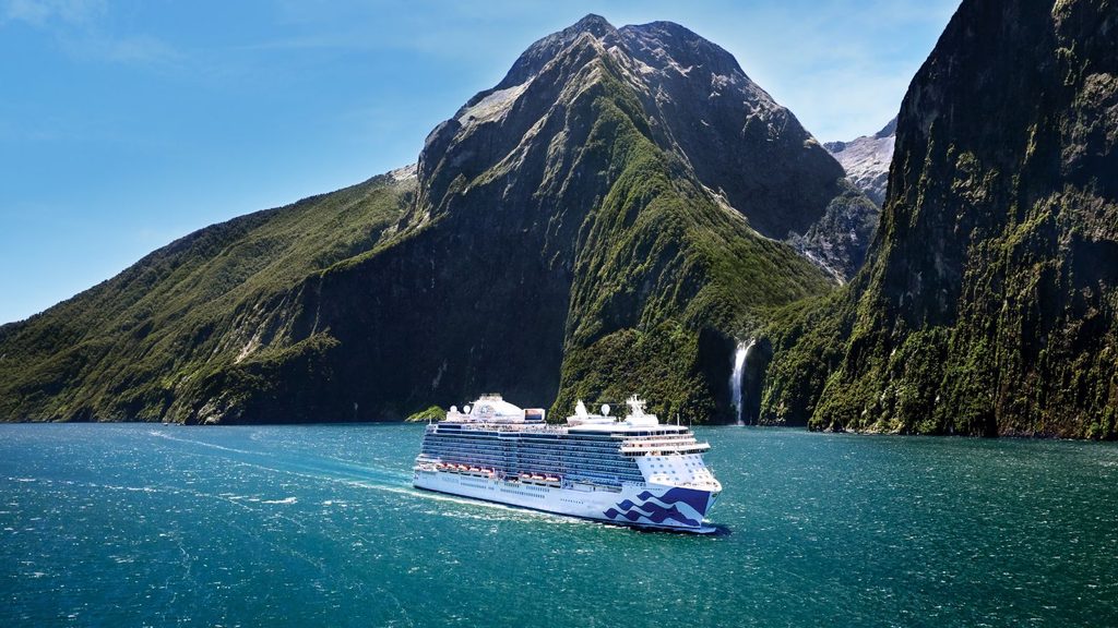 A cruise ship sailing on the water in front of a mountain with a waterfall.