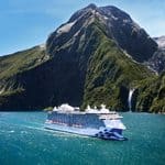 A cruise ship sailing on the water in front of a mountain with a waterfall.