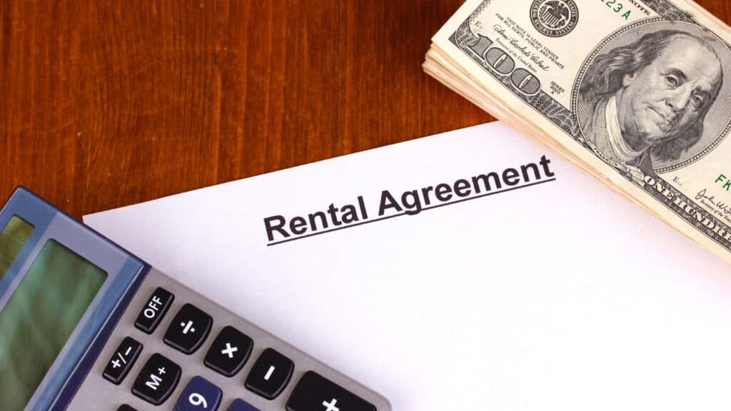 A rental agreement document next to a calculator and a stack of hundred-dollar bills, suggesting a potential timeshare scam.