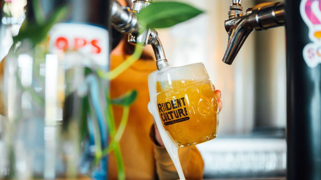 A beer tap pouring a golden ale from one of the Charlotte breweries into a glass with the Resident Culture Brewing Company logo.