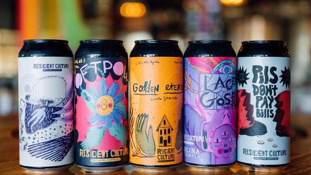 Five different Resident Culture Brewing Company beer cans from one of the popular Charlotte breweries lined up on a wooden surface.