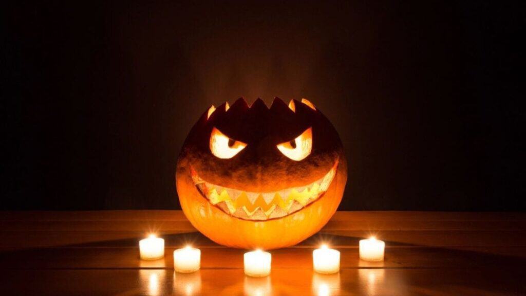 A jack-o’-lantern with a jagged, menacing face, illuminated from within and surrounded by five small, potential fire hazard candles on a wooden surface.
