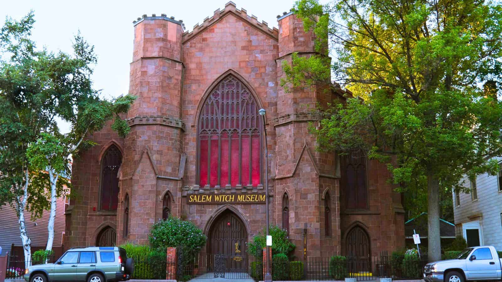 The Salem Witch Museum, a historic stone building with a large arched window, surrounded by trees.