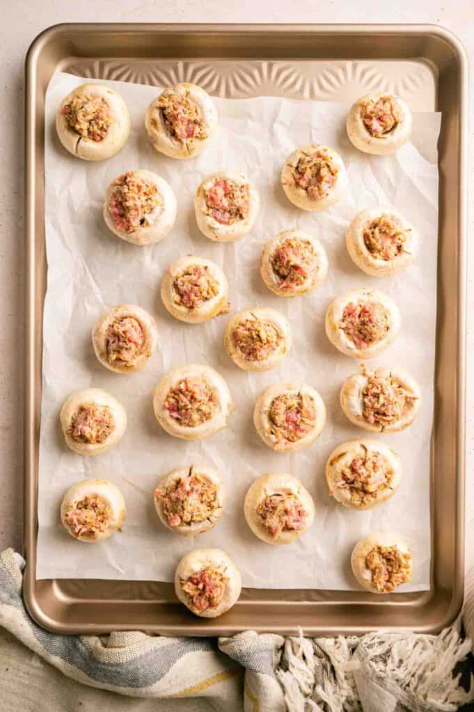 Mushroom caps stuffed with a savory filling arranged on a parchment-lined baking sheet.