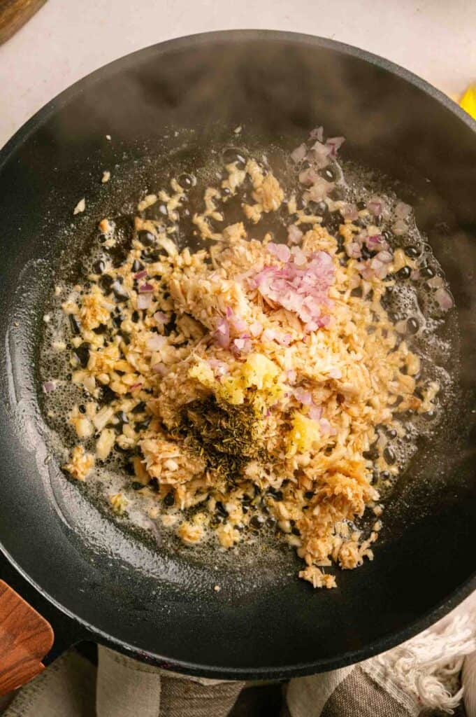 Minced garlic, shallots, and dried herbs sizzling in butter in a frying pan.