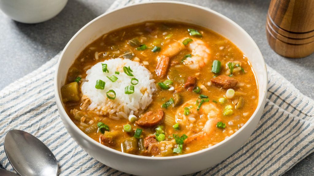 A bowl of shrimp and sausage gumbo topped with a scoop of white rice and chopped green onions.