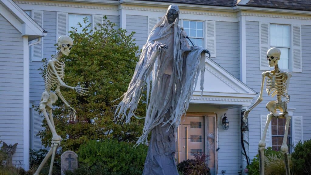 A tall, shrouded phantom stands between two skeletons in front of a house, creating a scene that tests the limits of HOA Halloween rules.