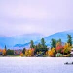 Two people in a canoe on a lake, framed by a village and autumn-colored trees perfect for fall-themed hotel packages in front of distant mountains.
