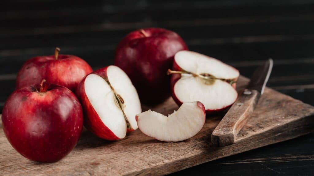 Red apples suitable for baking and eating fresh sit on a wooden cutting board, with one apple sliced and a paring knife nearby.