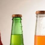 Three glass bottles of hard to find regional sodas filled with red, green, and orange liquid, all covered in condensation.