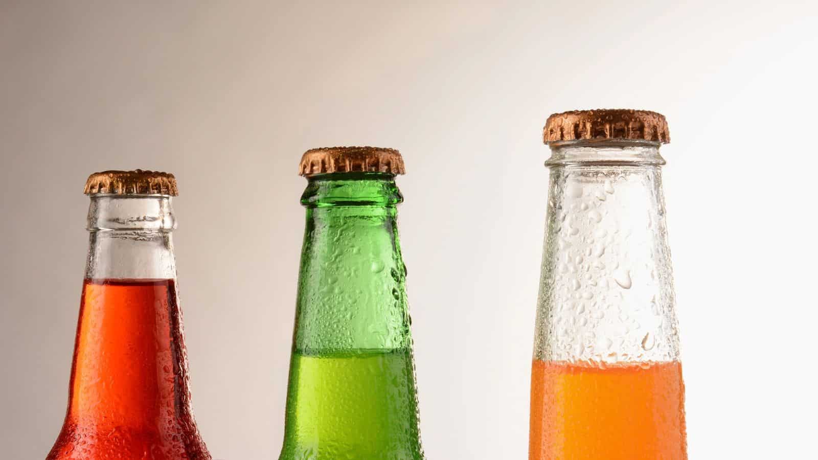 Three glass bottles of hard to find regional sodas filled with red, green, and orange liquid, all covered in condensation.