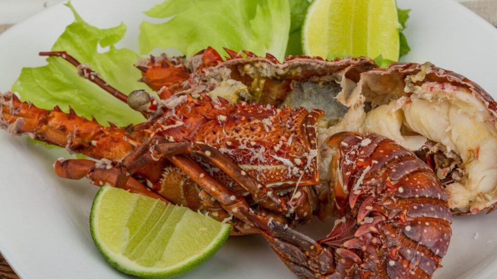 A cooked lobster tail from the Saba Rum and Lobster Fest served on a bed of lettuce with lime wedges.