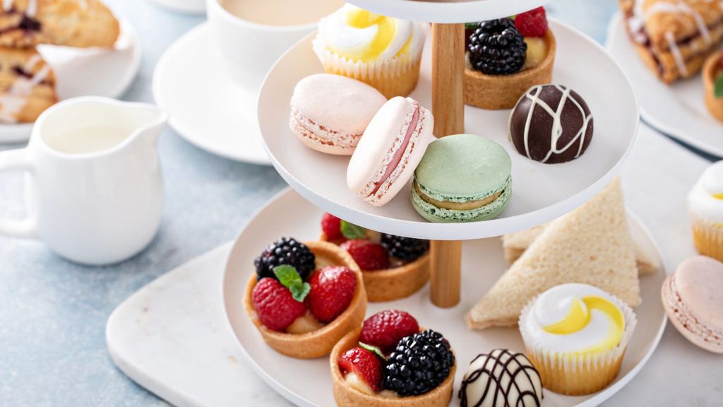 A two-tiered serving stand filled with assorted fruit tarts, macarons, chocolate truffles, cupcakes, and tea sandwiches perfect for National Dessert Day.