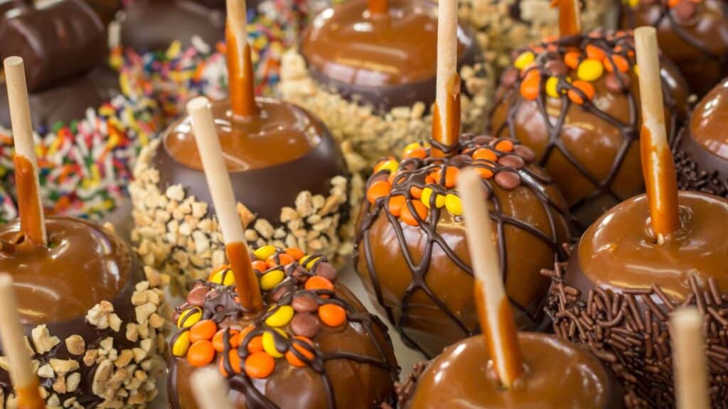 Several caramel apples on sticks dipped in chocolate and finished with caramel apple toppings like nuts, sprinkles, and colorful chocolate candies.
