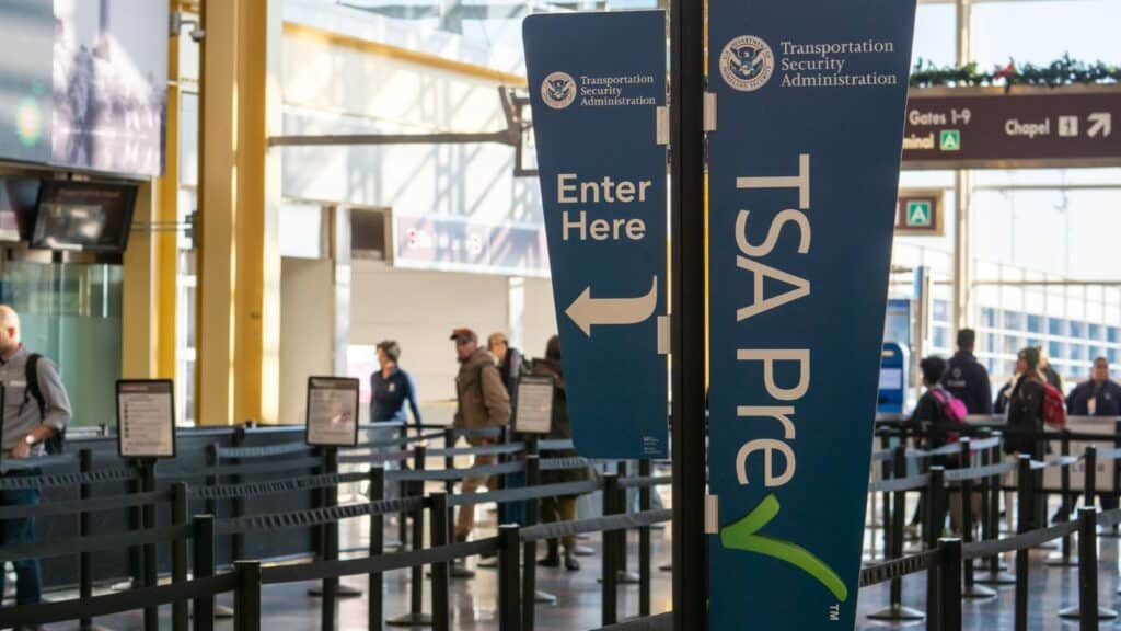 TSA PreCheck and Enter Here signs at an airport security checkpoint for a domestic flight.