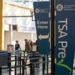 TSA PreCheck and Enter Here signs at an airport security checkpoint for a domestic flight.