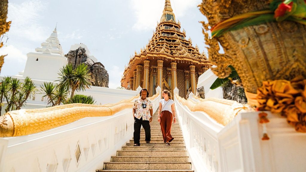 Two people walk down the stairs of a golden temple complex in Thailand, an iconic destination for luxury travel 2027.