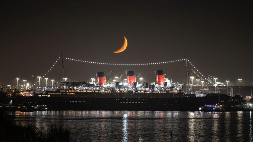 The Queen Mary, one of the world&rsquo;s most famous haunted hotels, is moored at night beneath a crescent moon.