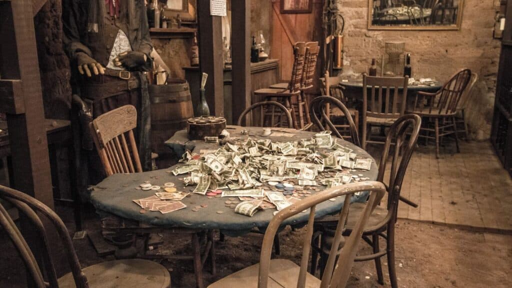 A poker table in a rustic room for a spookiest small-town fall road trip, covered in a pile of paper money and gaming chips, with a mannequin in western attire standing nearby.