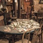 A poker table in a rustic room for a spookiest small-town fall road trip, covered in a pile of paper money and gaming chips, with a mannequin in western attire standing nearby.