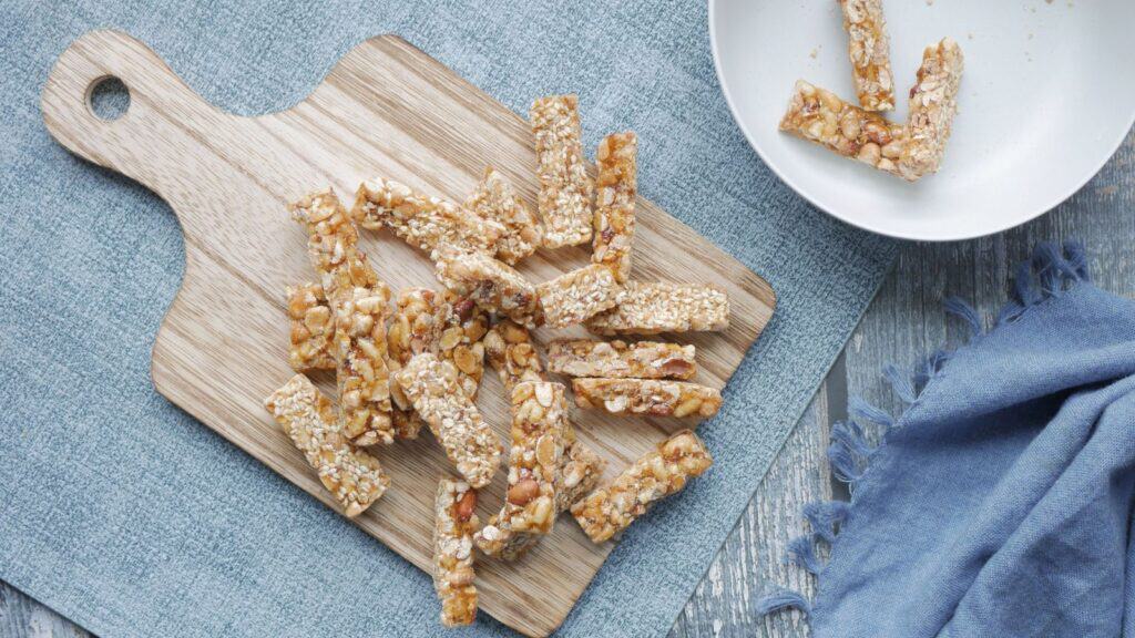 Nut and seed bars arranged on a wooden cutting board, with a few additional trunk-or-treat snack ideas in a white bowl nearby.