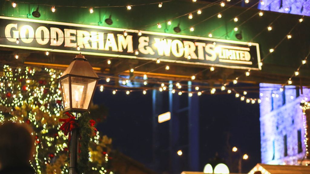 A sign reading &ldquo;Gooderham & Worts Limited&rdquo; illuminated by strings of lights above a street lamp at the Distillery Winter Village at night.