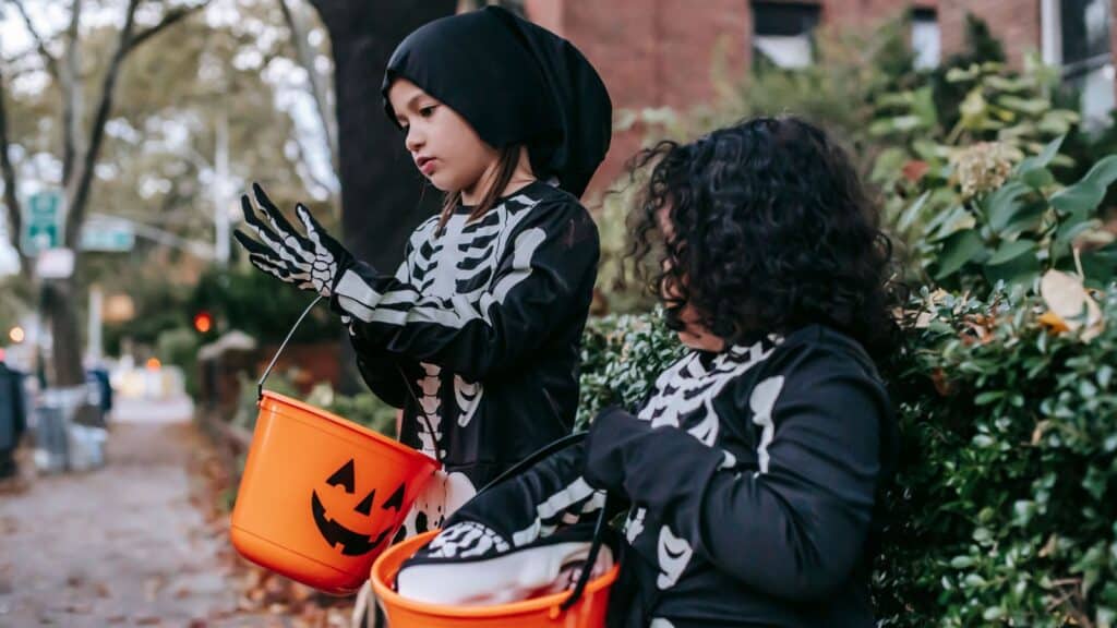 Two children in skeleton costumes hold pumpkin buckets while trick-or-treating, following Halloween safety rules for parents.