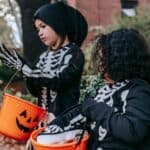 Two children in skeleton costumes hold pumpkin buckets while trick-or-treating, following Halloween safety rules for parents.