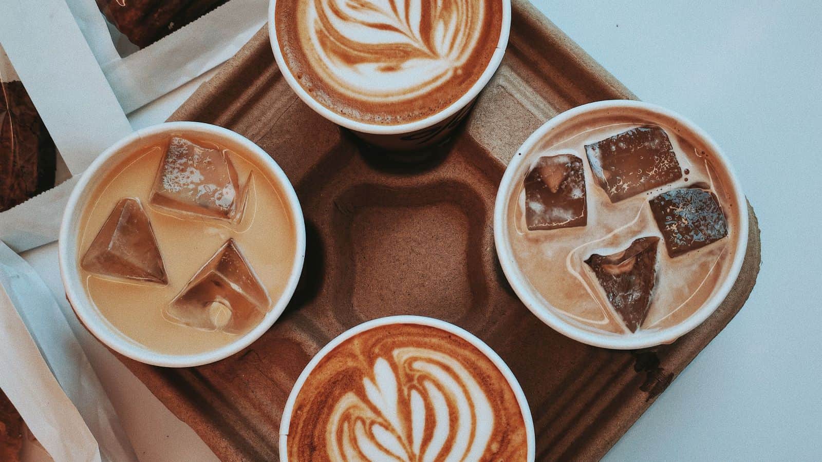A cardboard drink carrier holding a fall coffee switch of two iced coffees and two lattes with latte art.
