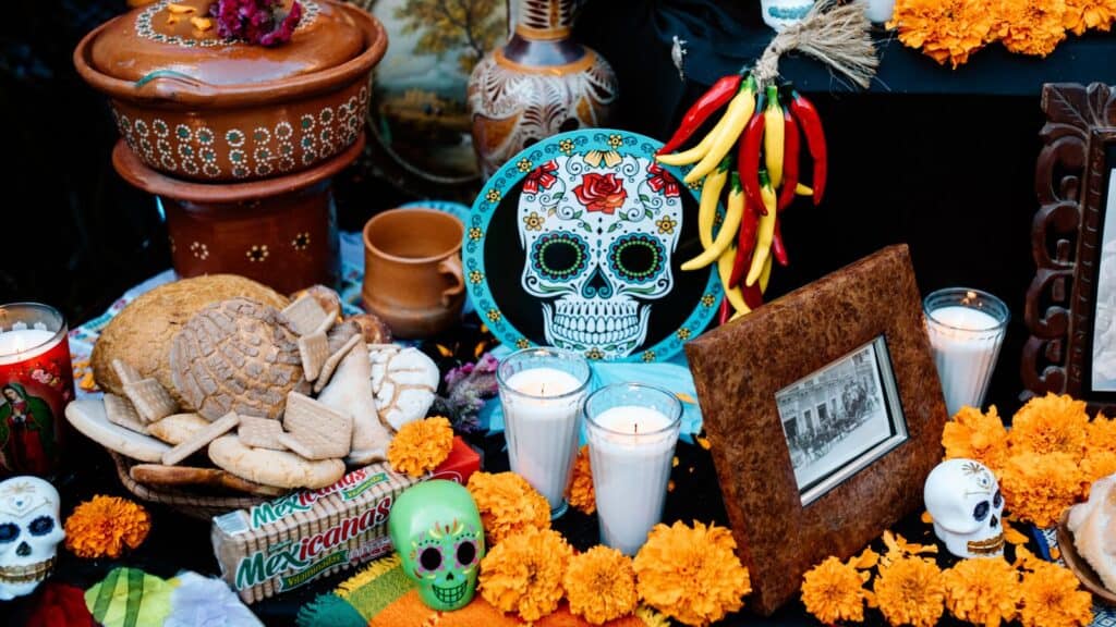 D&iacute;a de los Muertos altar with marigolds, candles, sugar skulls, a ceramic bowl, and food offerings, representing countries with Halloween-like traditions.