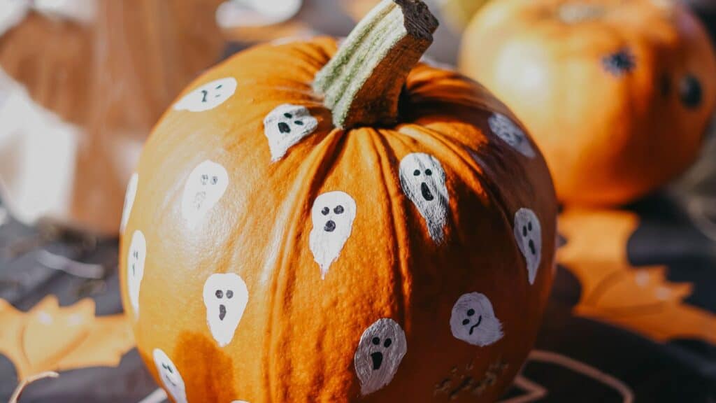 An orange pumpkin decorated with several hand-painted white ghosts, showcasing creative pumpkin carving techniques.