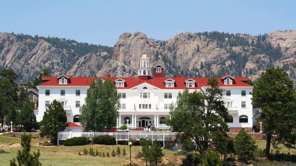 The Stanley Hotel, one of the most famous haunted hotels and inns, features a red roof and white fence set against a backdrop of rocky mountains.