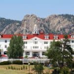The Stanley Hotel, one of the most famous haunted hotels and inns, features a red roof and white fence set against a backdrop of rocky mountains.