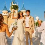 A bride and groom pose for photos in front of a castle-themed building as wedding guests capture the moment at a destination offering Caribbean wedding packages.