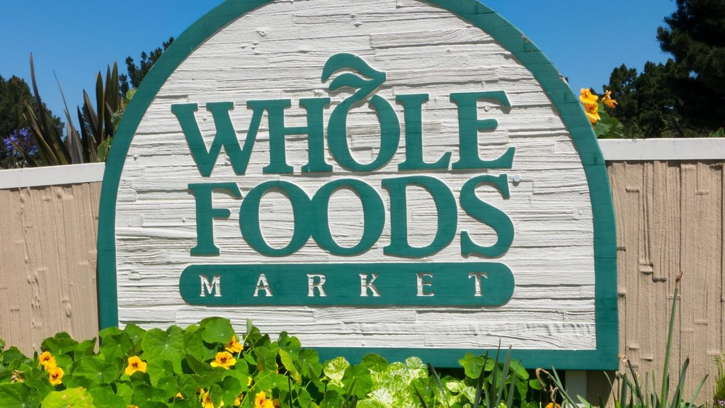 A Whole Foods Market sign surrounded by green plants and yellow flowers.
