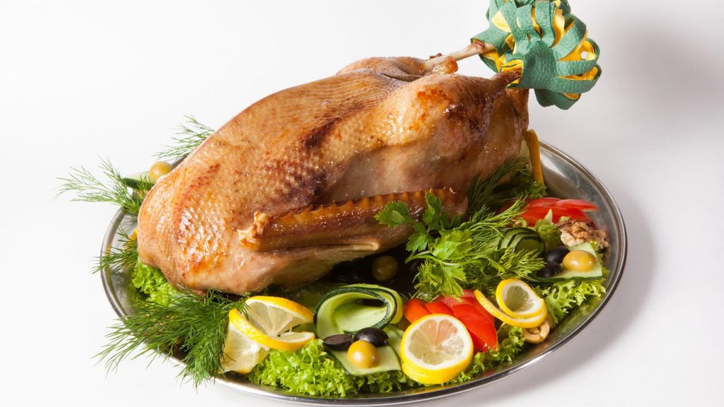 Roasted whole duck on a silver platter garnished with lettuce, dill, lemon slices, olives, and tomatoes.
