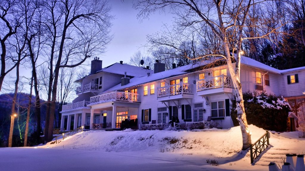 A white multi-story hotel with lit balconies and windows at twilight, surrounded by a snowy landscape and bare trees.