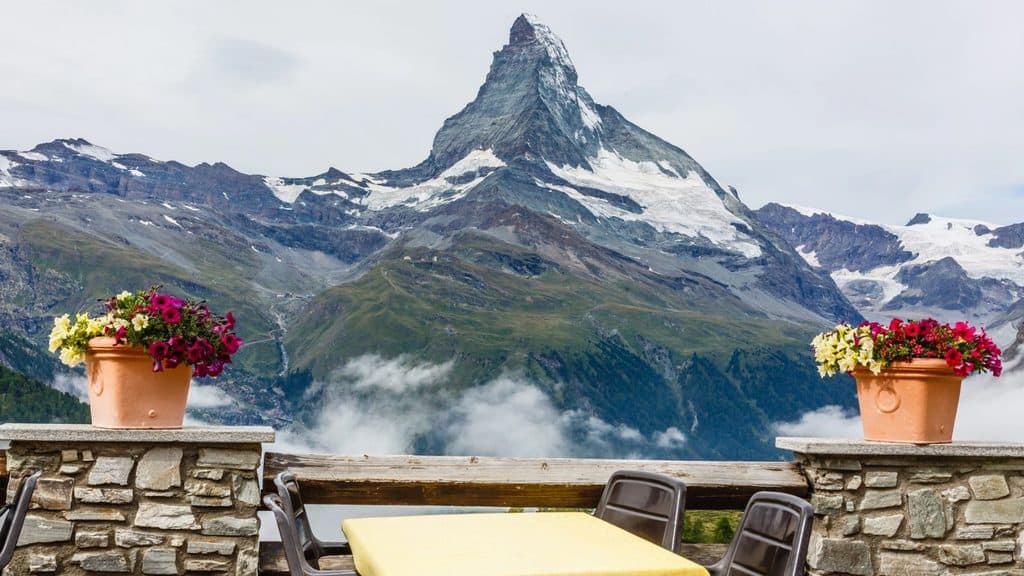View of the Matterhorn from a stone terrace with two flower pots and a dining table.
