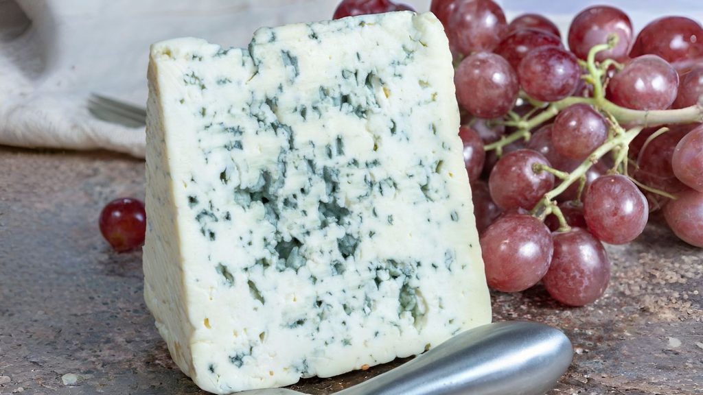 A wedge of blue cheese next to a cluster of red grapes.