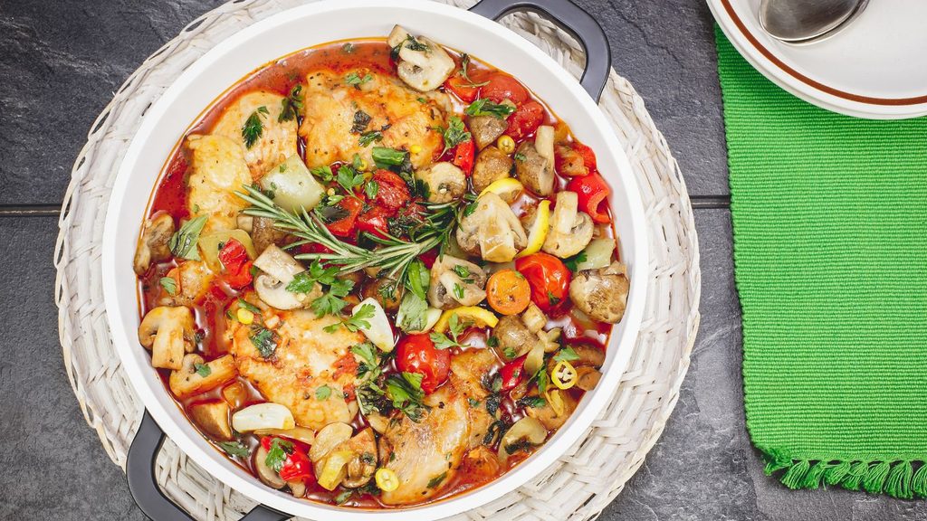 Casserole dish of chicken cacciatore, featuring thighs braised with mushrooms, cherry tomatoes, and fresh herbs.