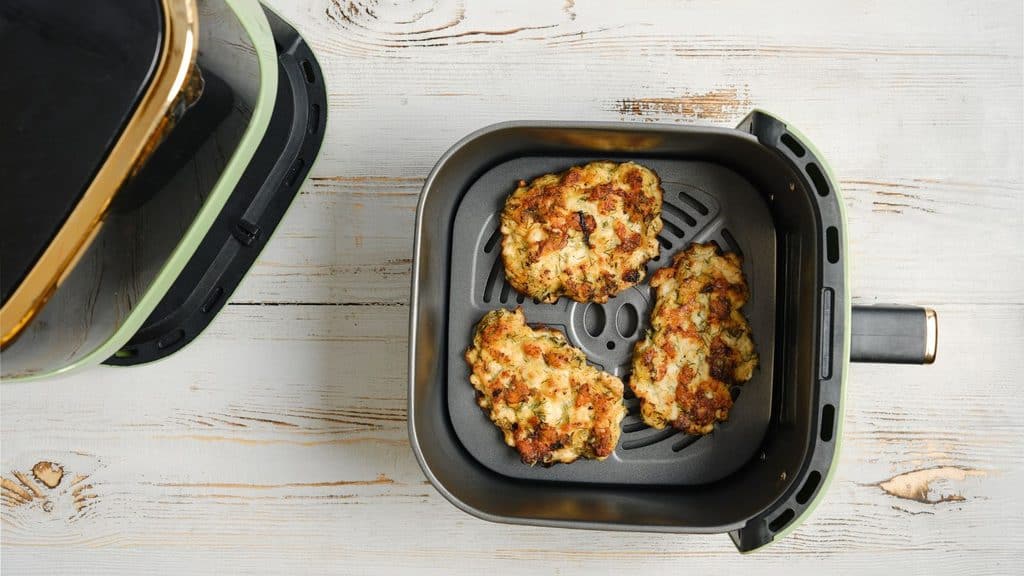 Three browned patties cooking in an air fryer basket.