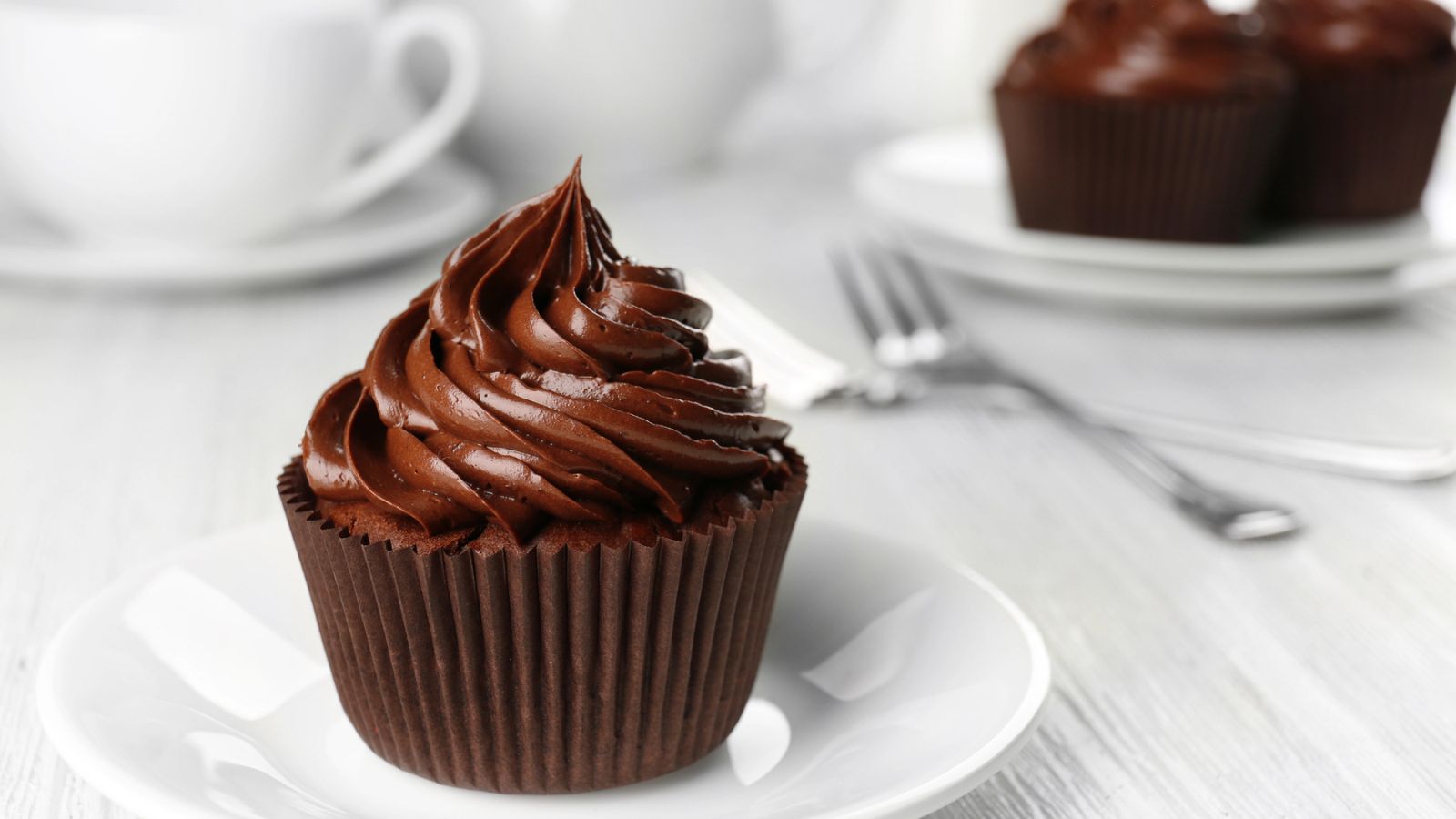 A chocolate cupcake with chocolate frosting on a small white plate.