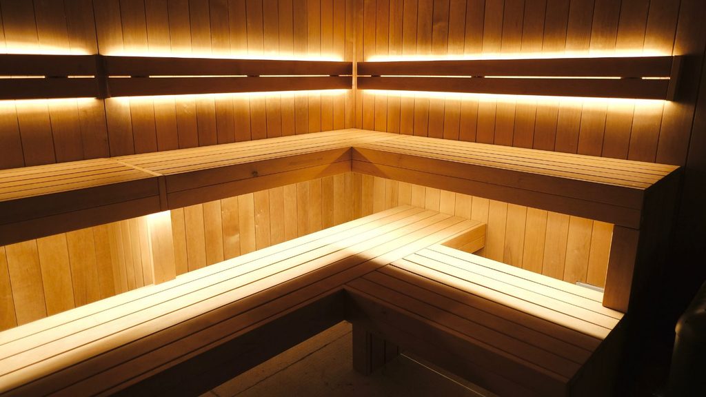 Empty wooden sauna interior with tiered bench seating and integrated warm LED strip lighting.