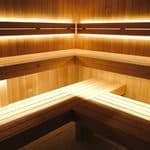 Empty wooden sauna interior with tiered bench seating and integrated warm LED strip lighting.