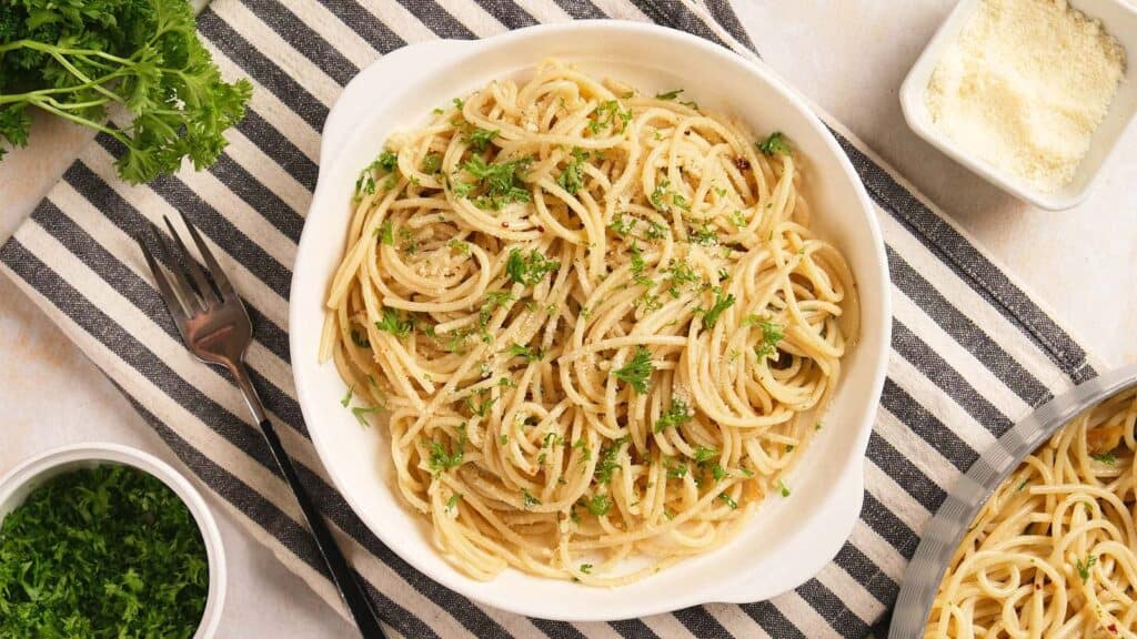 A bowl of spaghetti topped with grated cheese and fresh parsley, served with side dishes of cheese and herbs.