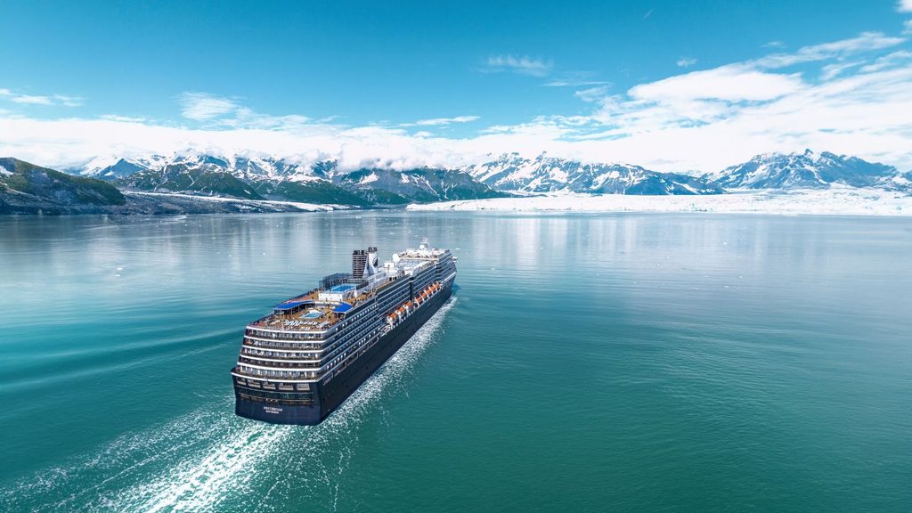 A cruise ship sailing on a calm bay in front of a glacier and snow-capped mountains.