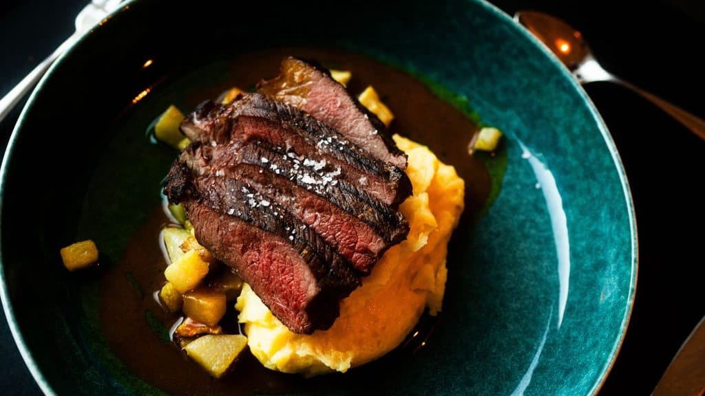 Sliced seared steak topped with sea salt, served over mashed potatoes and saut&eacute;ed vegetables in a dark sauce.