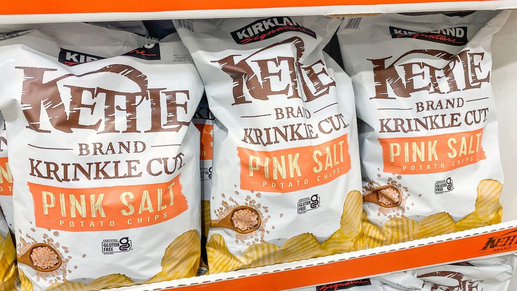 Three bags of Kirkland Signature Kettle Brand krinkle cut pink salt potato chips on a store shelf.